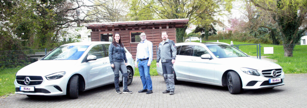 Führungsteam im Hintergrund zwei Mercedes-Benz Firmenfahrzeuge